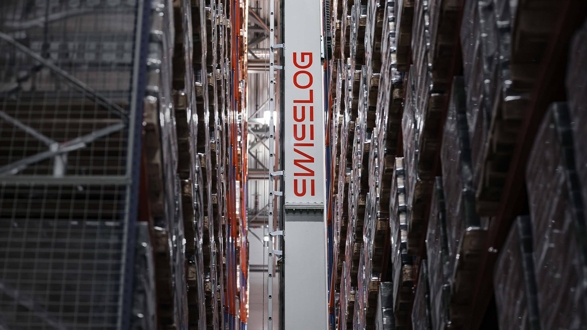 Automated high-bay warehouse aisle with Swisslog Vectura stacker crane handling palletized goods