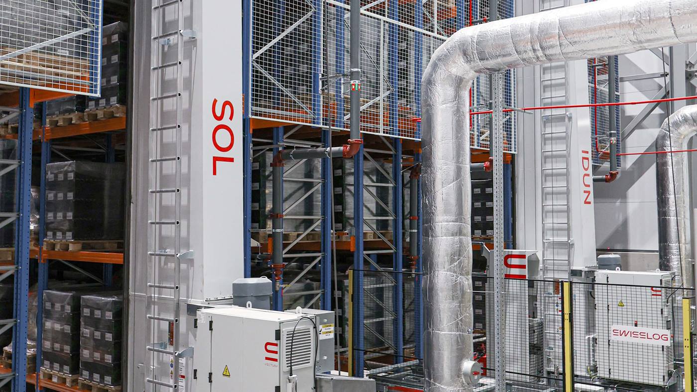 Swisslog automated high-bay warehouse with pallet racking, conveyors, stacker cranes, and material handling equipment