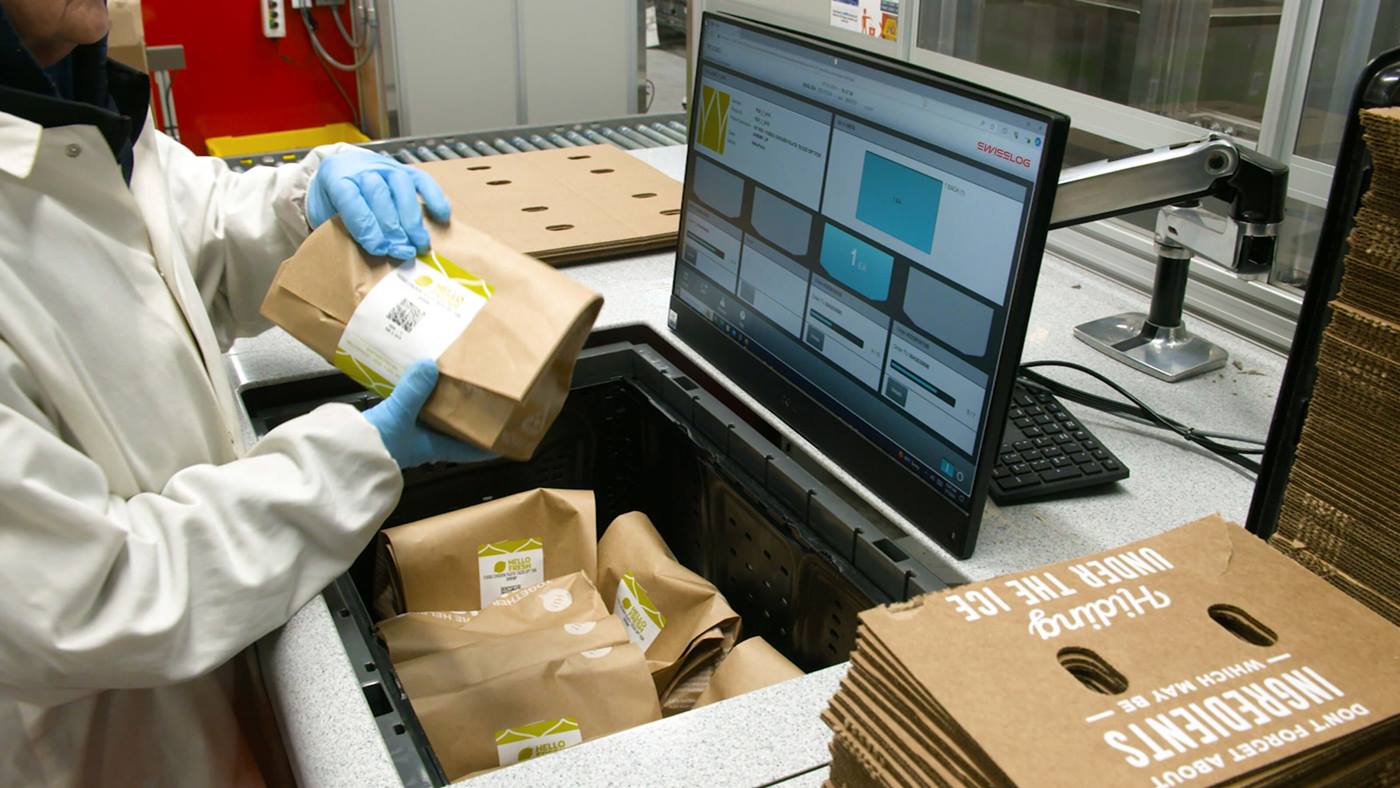 Warehouse employee at HelloFresh distribution center using Swisslog's SynQ WMS to manage inventory at an AutoStore picking port.
