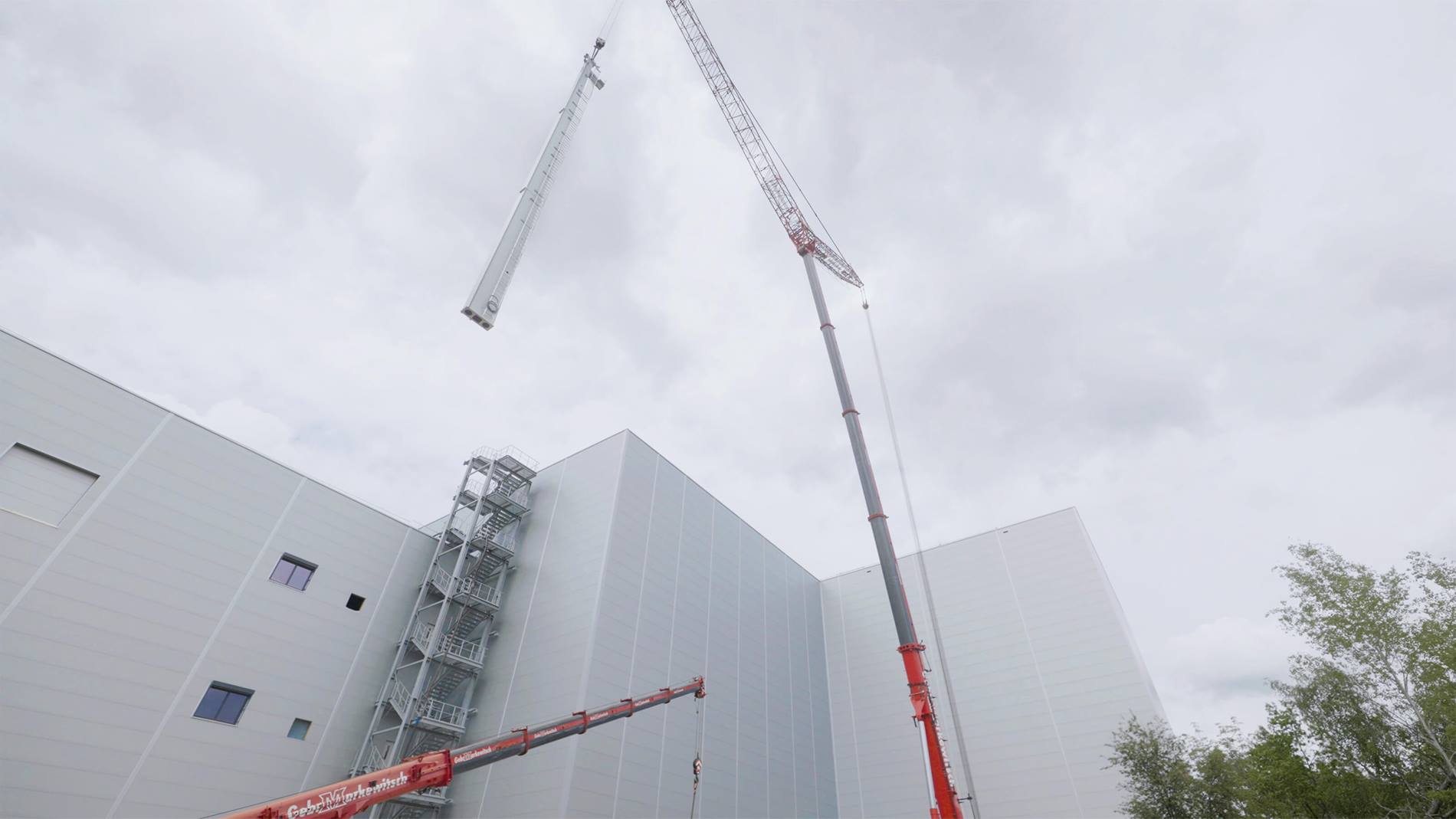 Crane installing Vectura pallet stacker crane mast at automated high-bay warehouse exterior