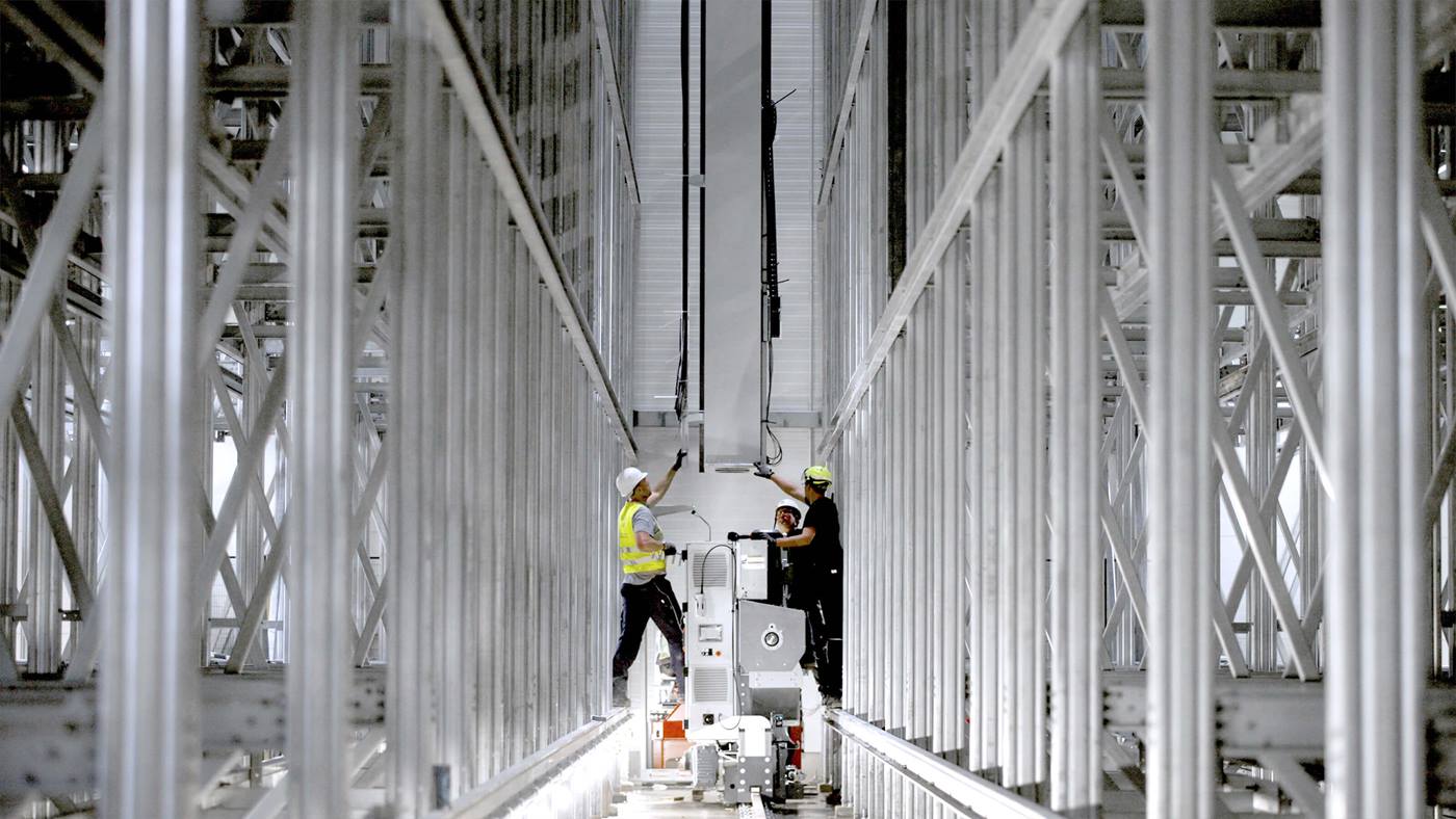 Technicians installing Vectura pallet stacker crane between racking in automated high-bay warehouse