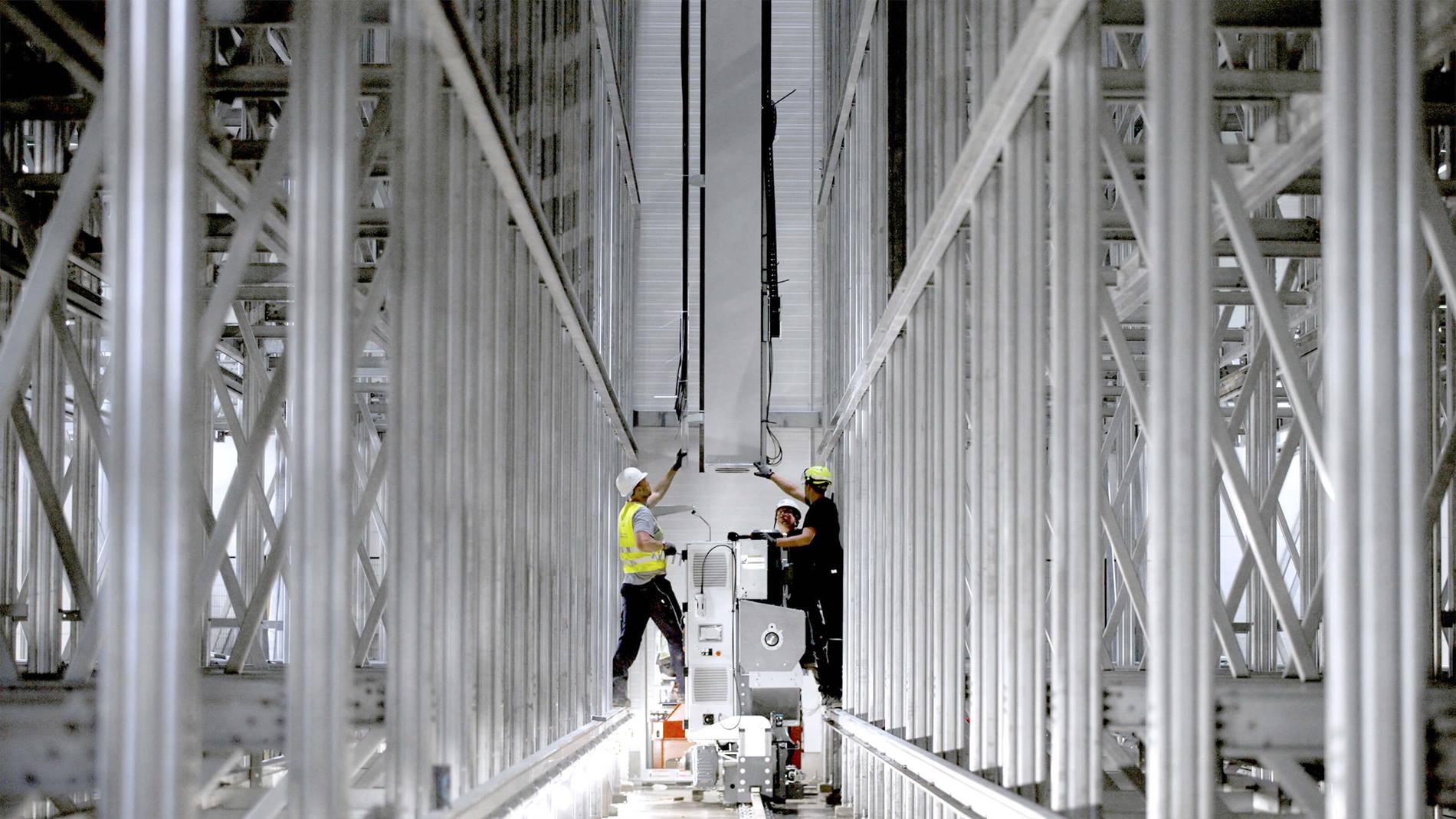 Technicians installing Vectura pallet stacker crane between racking in automated high-bay warehouse