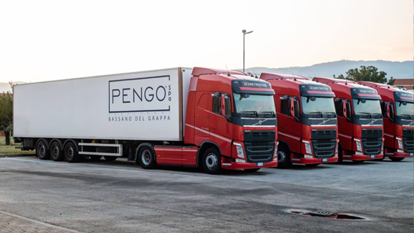 Fleet of red Volvo trucks parked in a lot, with the lead truck displaying a white trailer labeled 'PENGO S.P.A. BASSANO DEL GRAPPA'.