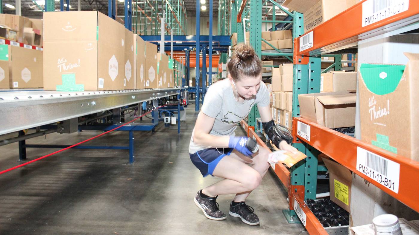 Thrive Market-Mitarbeiter tragen am Handgelenk montierte Bildschirme mit Finger-Scanner, um SKUs und Kartons zu identifizieren.