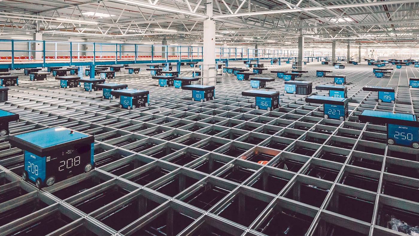 AutoStore system empowered by Swisslog featuring automated storage cubes on a grid in a large warehouse at Arvato's facility.